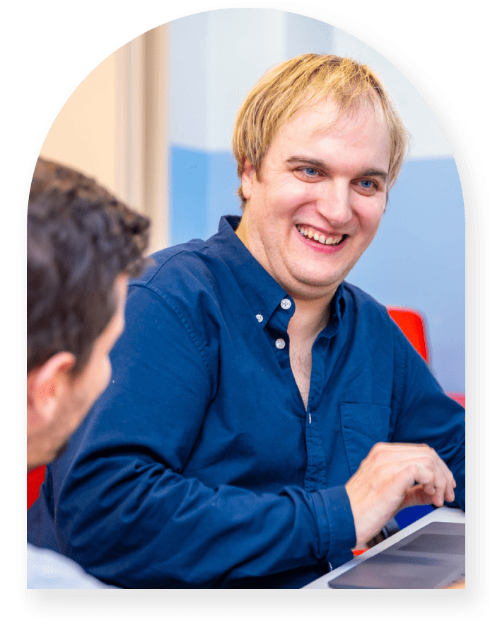 Smiling man in blue shirt working on laptop.